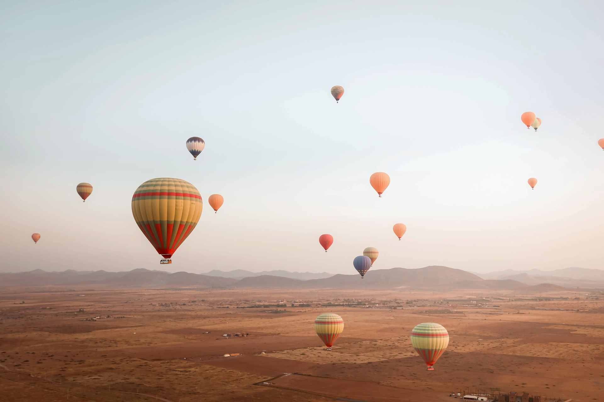Hot-air balloons drifting over the plains near Marrakech at sunrise, with the hills of the Atlas on the horizon