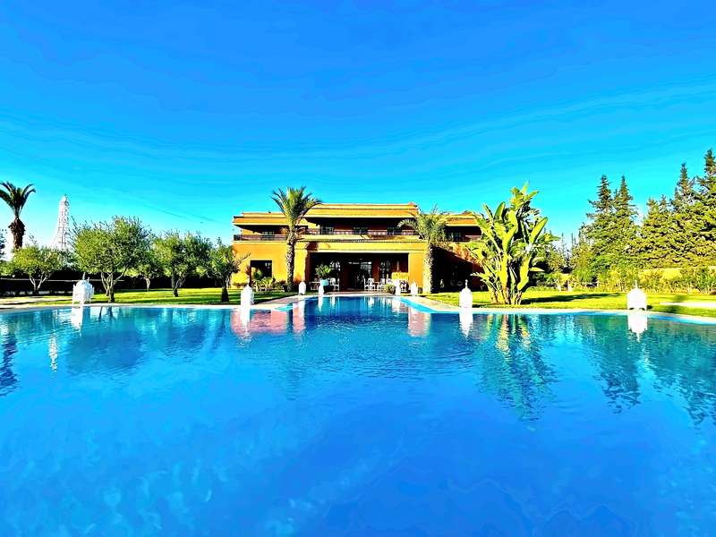 Very large pool in front of the two-storey terracotta villa, with palms, banana plants and white lanterns