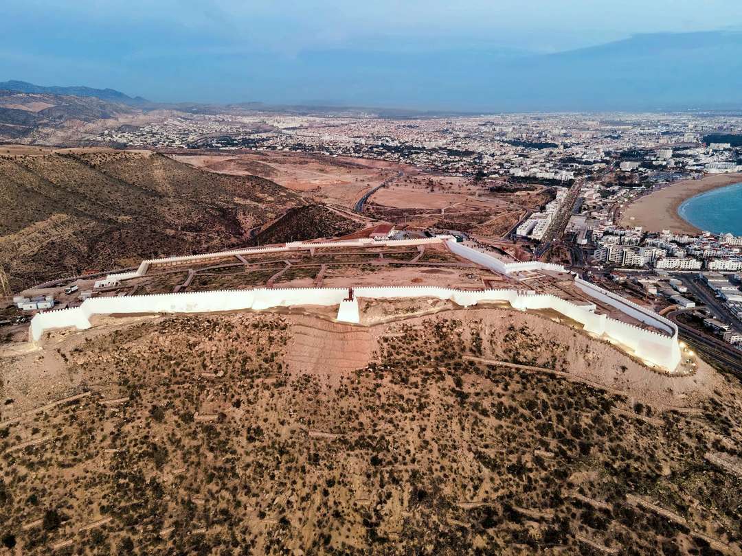 Les remparts blancs de la kasbah d’Agadir Oufella sur leur colline au crépuscule, la ville et la baie étalées en contrebas