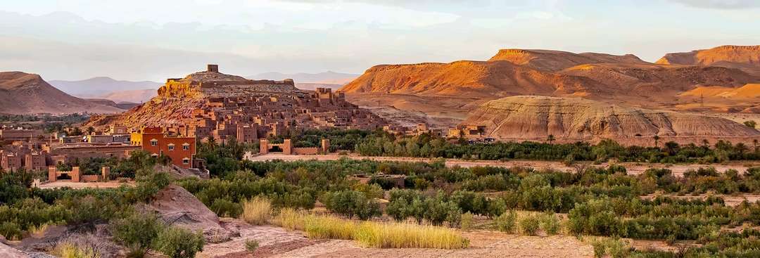 O ksar de Aït Ben Haddou na luz do fim da tarde, o oásis em frente e as colinas nuas e ocre do vale por trás