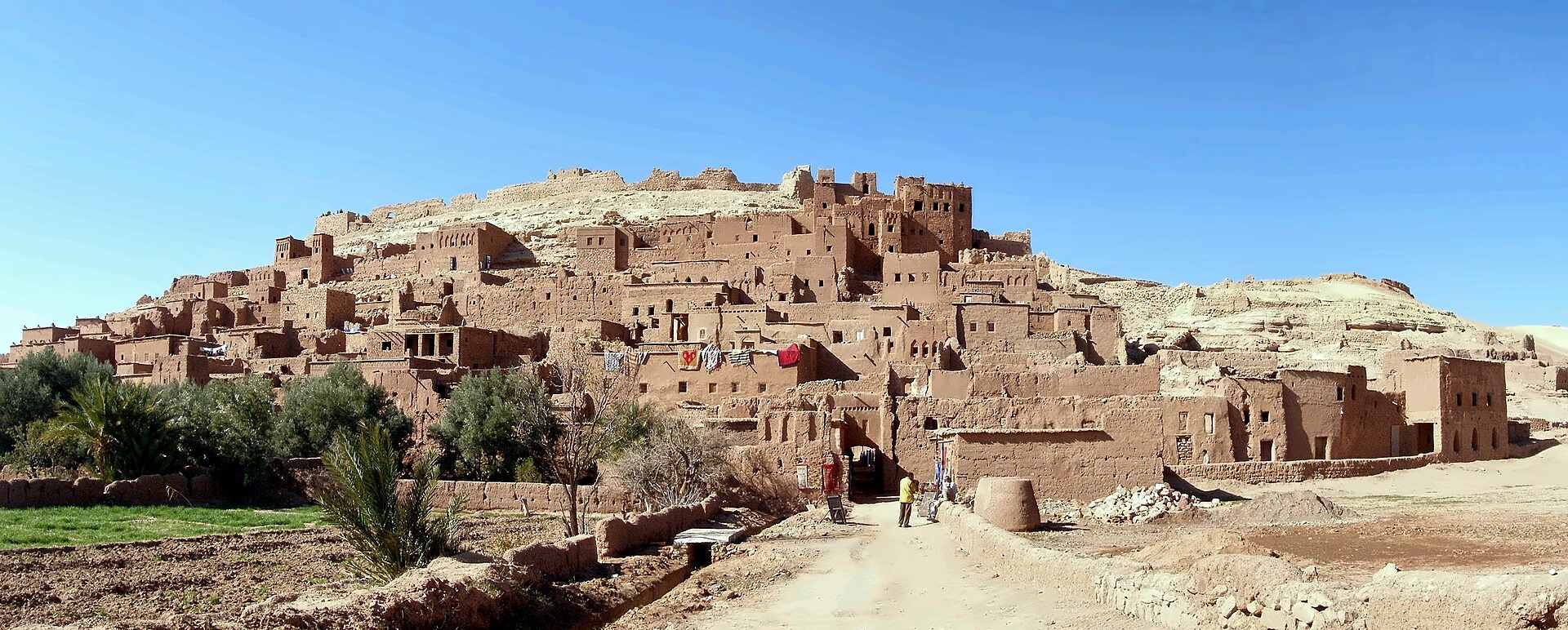 O ksar de terra de Aït Ben Haddou a erguer-se na sua colina acima do caminho, casas e torres empilhadas até ao celeiro no topo