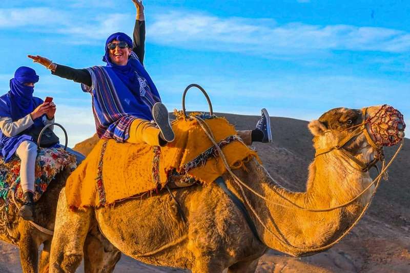 Viajeros con túnicas azules montados en camellos sobre el suelo pedregoso de las afueras de Marrakech