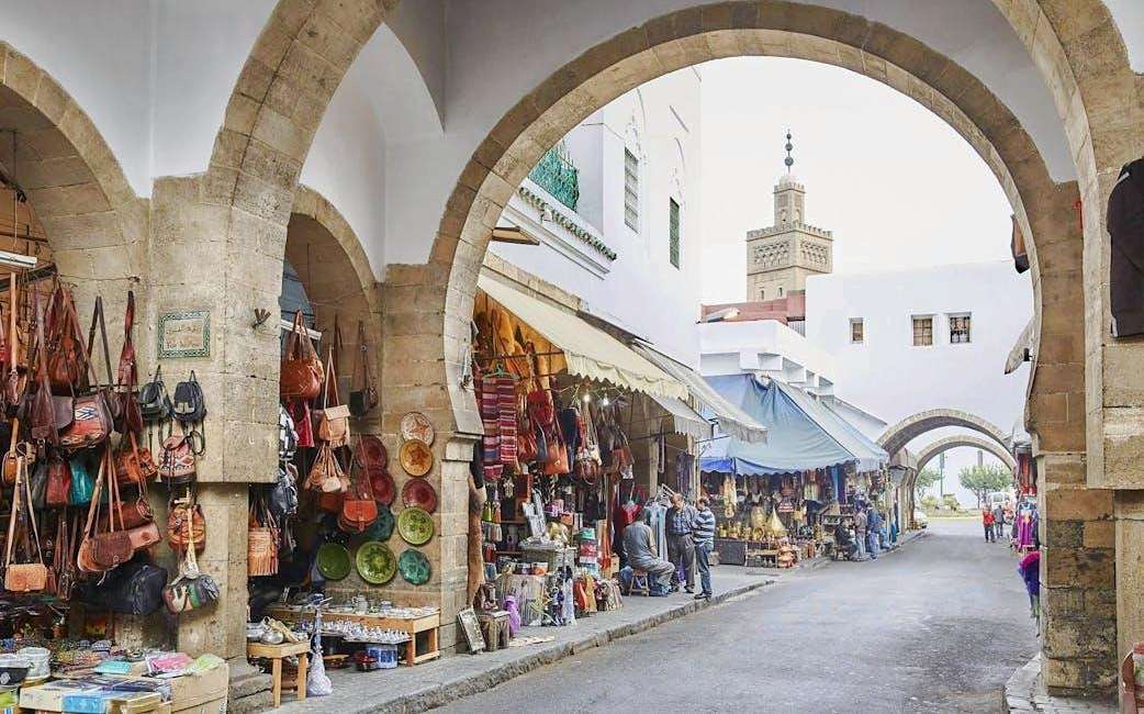 Arkadengassen mit Läden voller Ledertaschen und bemalter Keramik, hinter dem Torbogen ein gefliestes Minarett über den weißen Gebäuden