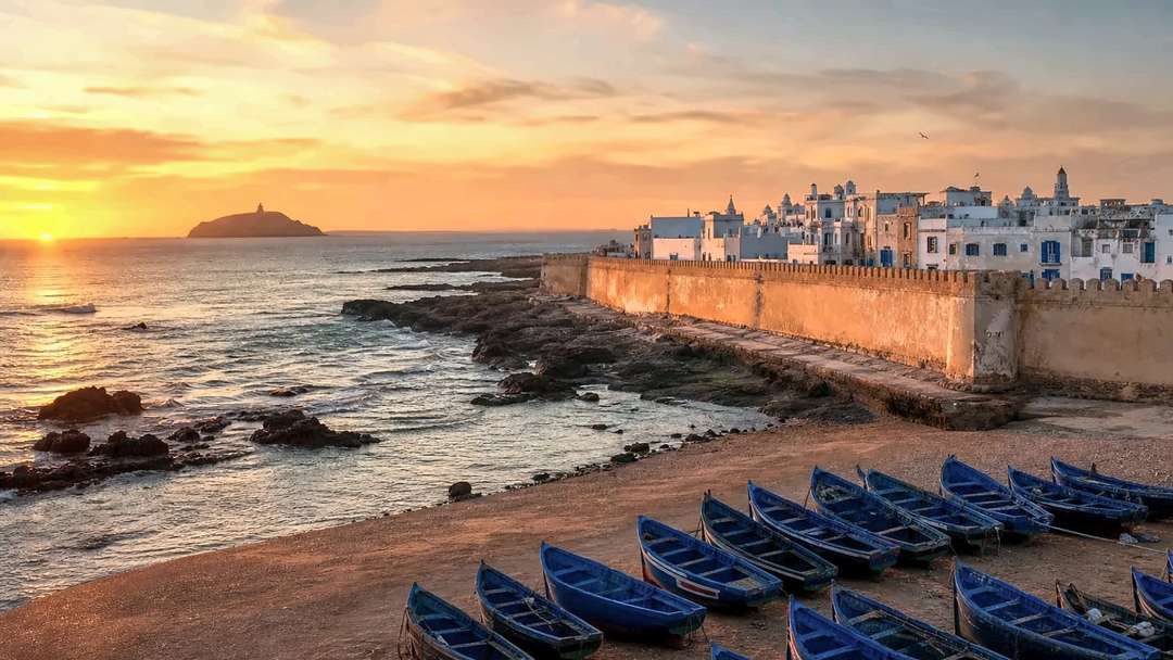 Zonsondergang boven de zee bij Essaouira, blauwe vissersboten op het zand getrokken onder de okerkleurige vestingmuren van de medina