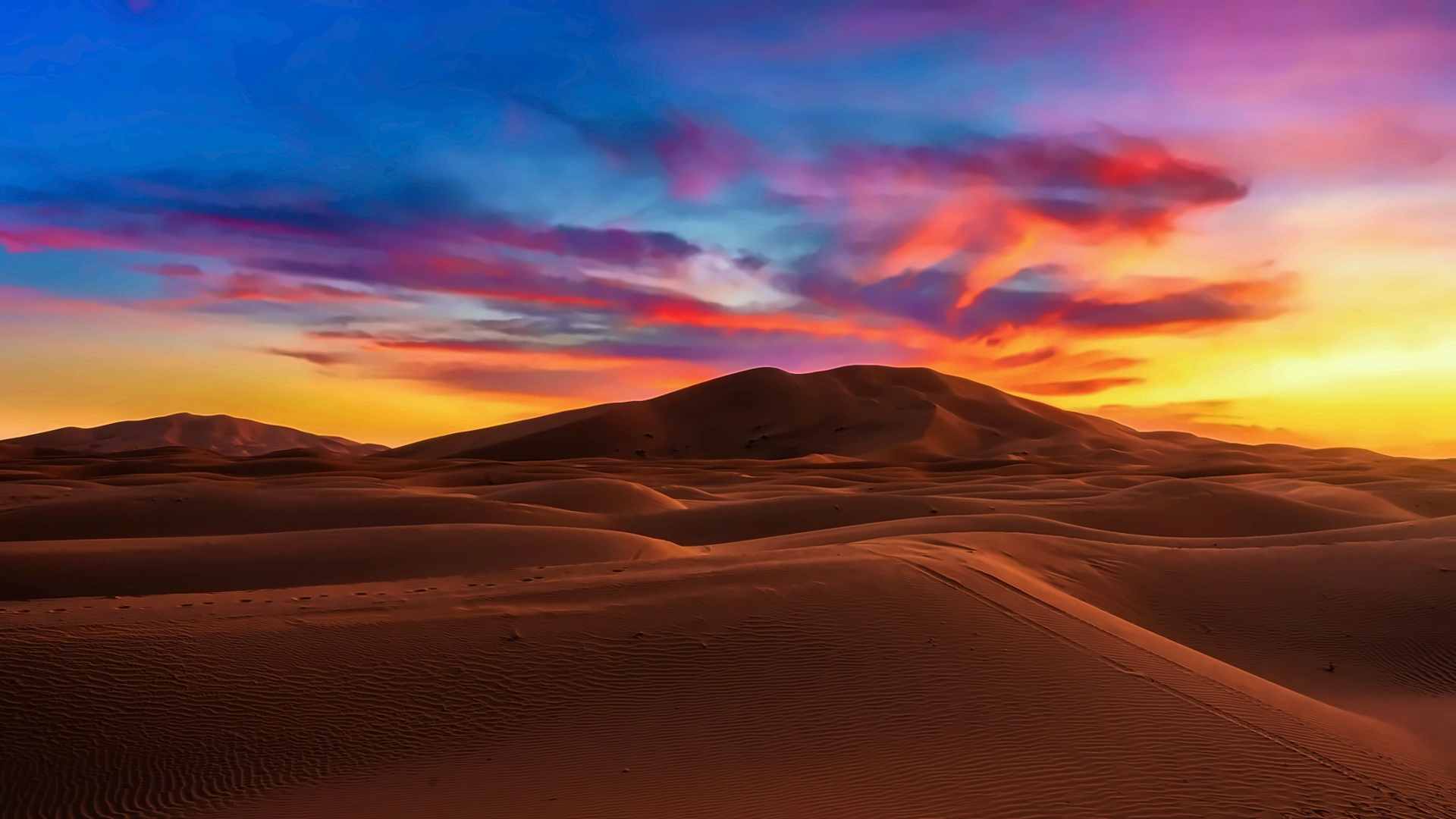 As dunas do Erg Chebbi ao pôr do sol, cristas de areia laranja a correr até ao horizonte sob um céu vermelho e violeta