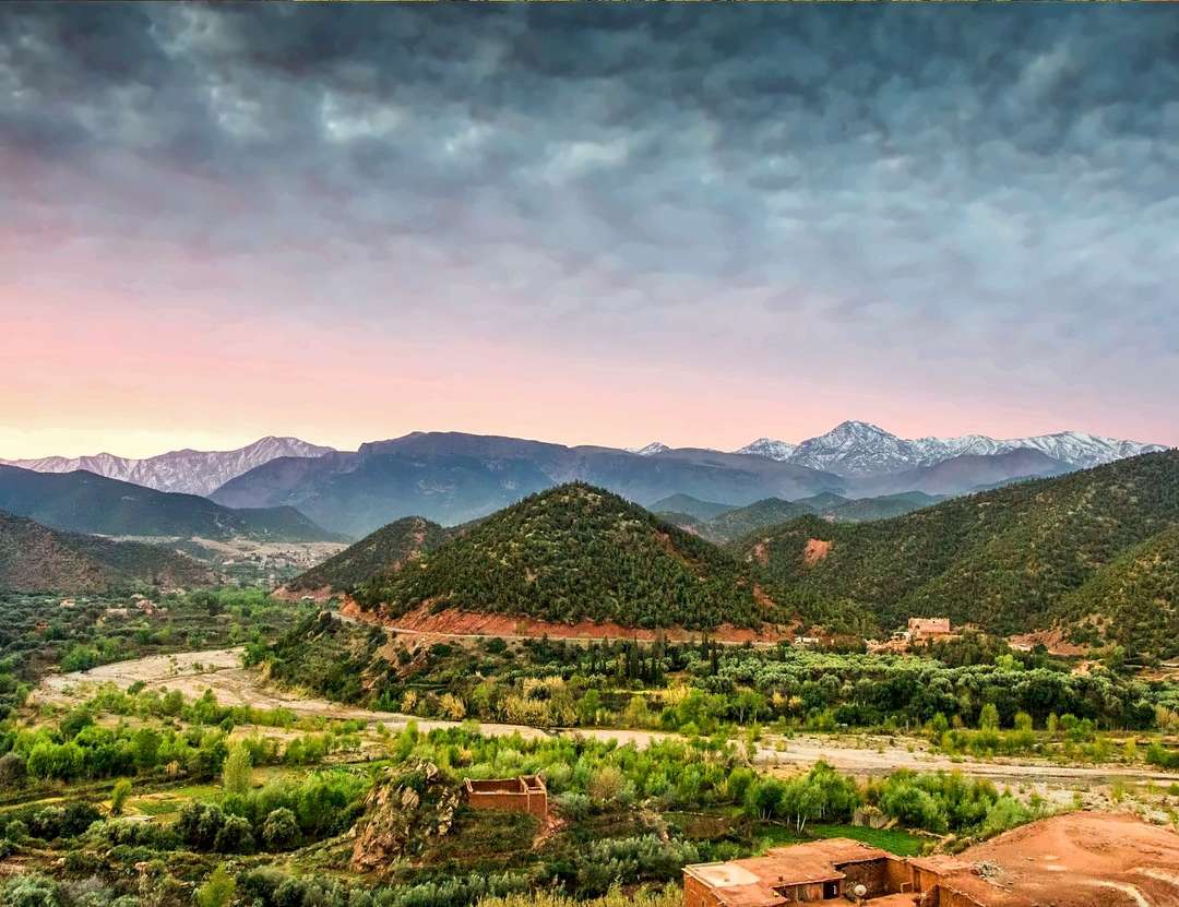 O vale do Ourika ao crepúsculo, um céu rosa sobre o Alto Atlas nevado e casas de terra entre as árvores