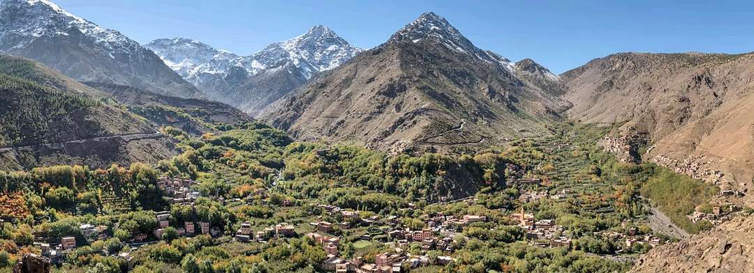 Veduta ampia lungo una valle verdeggiante bordata di villaggi e di terrazze, chiusa in fondo dalle vette innevate dell’Atlante