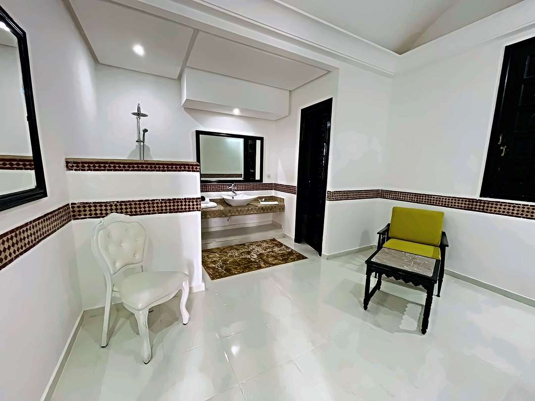 Bagno con fascia di zellige, doccia aperta, lavabo su piano di zellige e angolo salotto