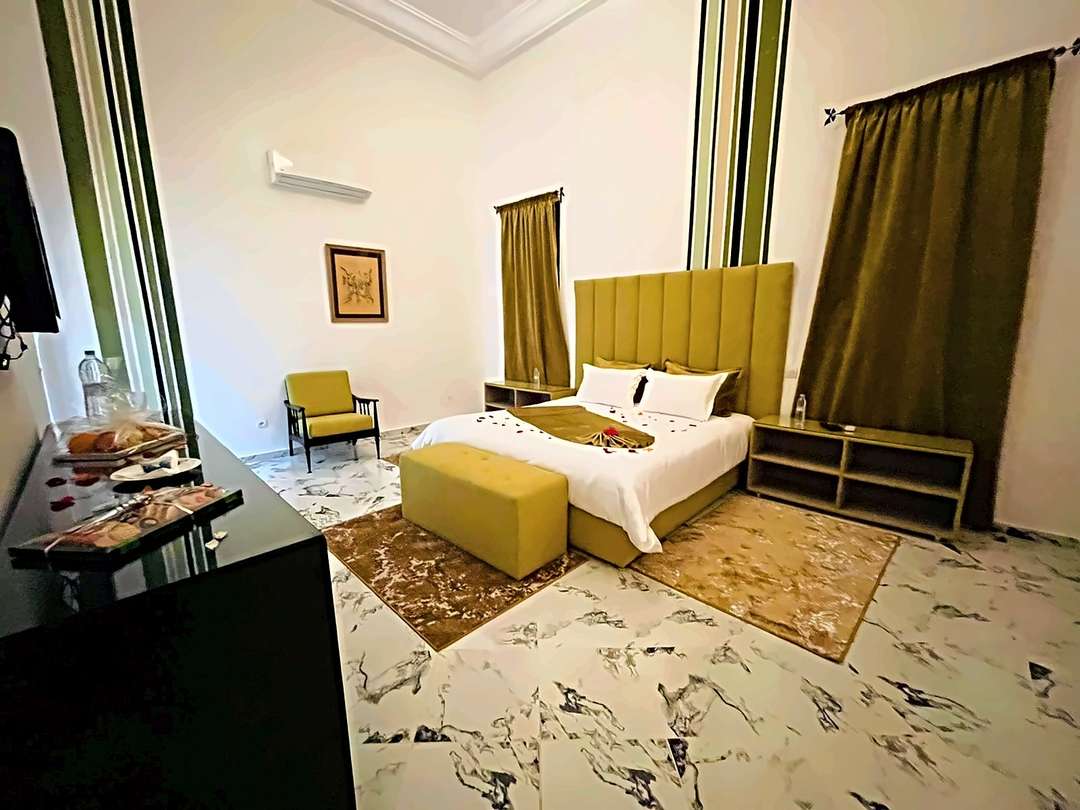 Camera con letto in velluto senape, panca, pareti a righe verdi e pavimento effetto marmo