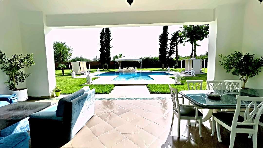 Terrazza coperta con divani blu e tavolo da pranzo, aperta sul prato e sulla piscina