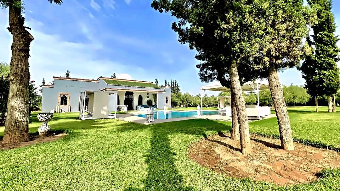 Villa con tetto di tegole verdi e cupola, vista al di là di un prato piantato di cipressi