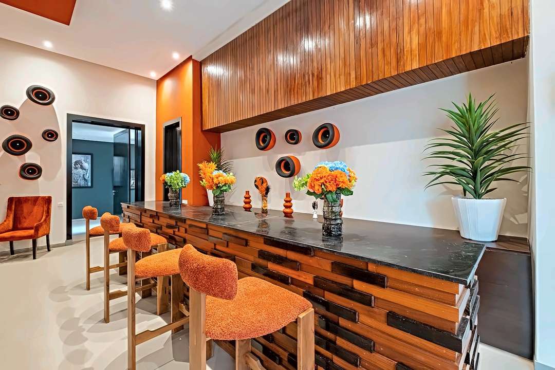 Bar mit Theke aus Altholz, orangen Bouclé-Hockern und einem Lattendach aus Holz
