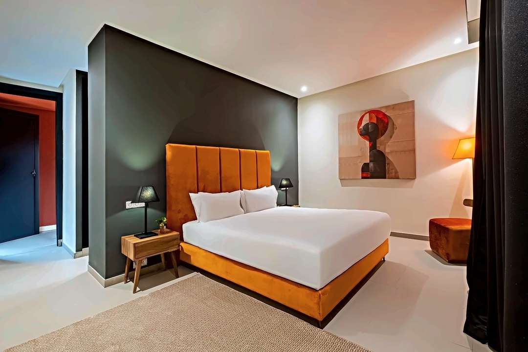 Schlafzimmer mit hohem Kopfteil in orangem Samt an anthrazitfarbener Wand und einem modernen Gemälde