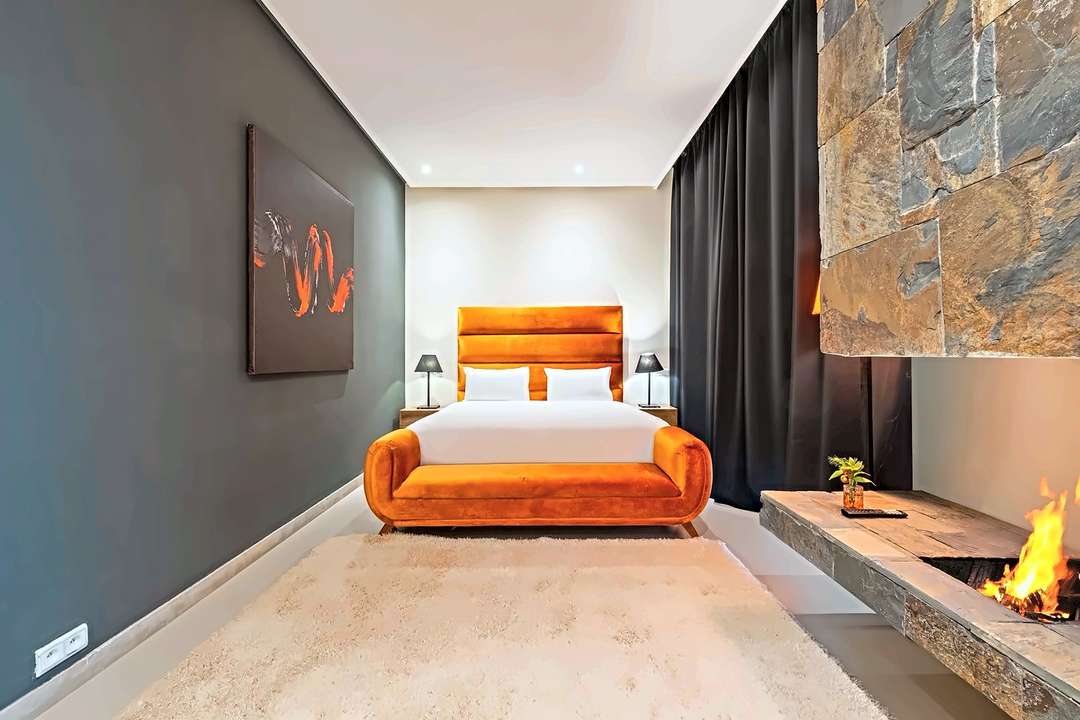 Schlafzimmer mit Kopfteil und Bank in orangem Samt, anthrazitfarbenen Wänden und Steinkamin