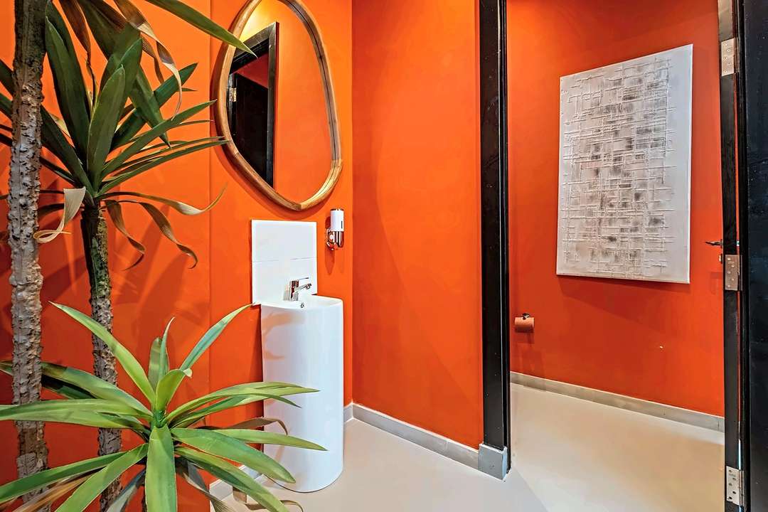 Gästebad mit orangen Wänden, weißem Standwaschbecken und einem Holzspiegel in organischer Form