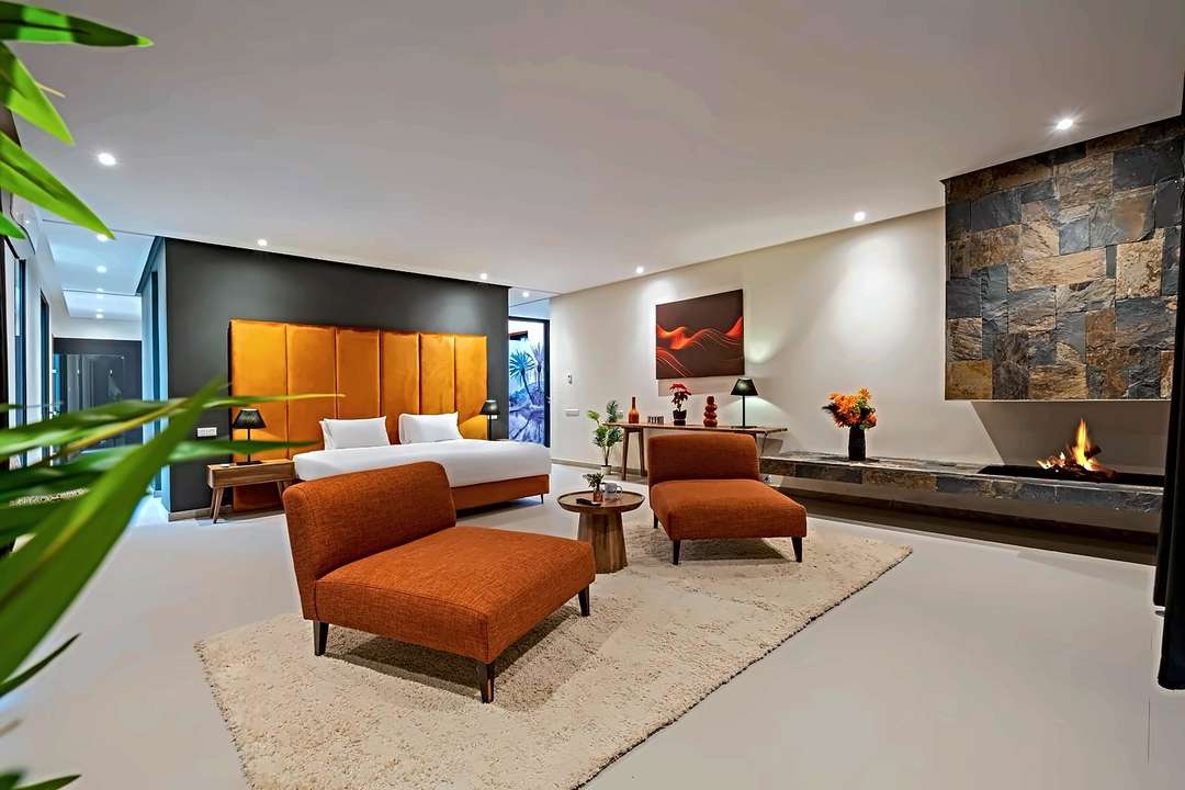 Hauptsuite mit Steinkamin, orangen Loungesesseln und einem wandhohen Kopfteil aus Samt