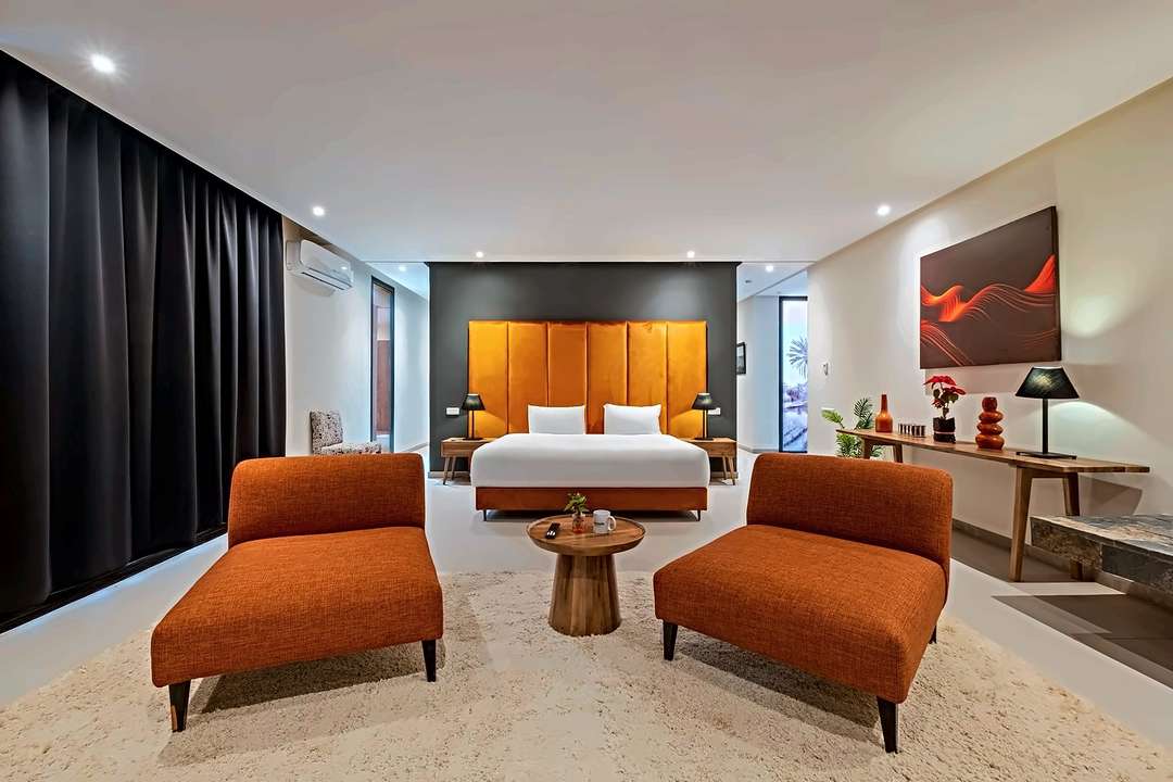 Hauptsuite mit hohem Kopfteil in orangem Samt, zwei orangen Loungesesseln und einem Schaffellteppich