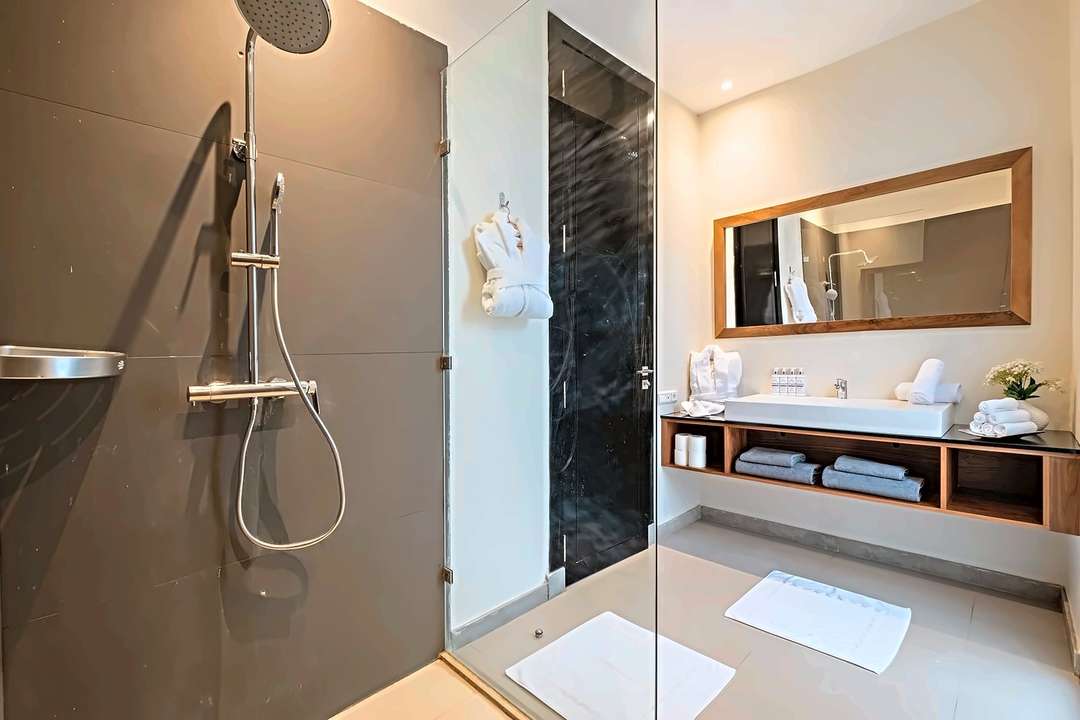 Duschbad mit Regendusche hinter einer Glasabtrennung, dunklen Steinwänden und Waschtisch aus Walnussholz