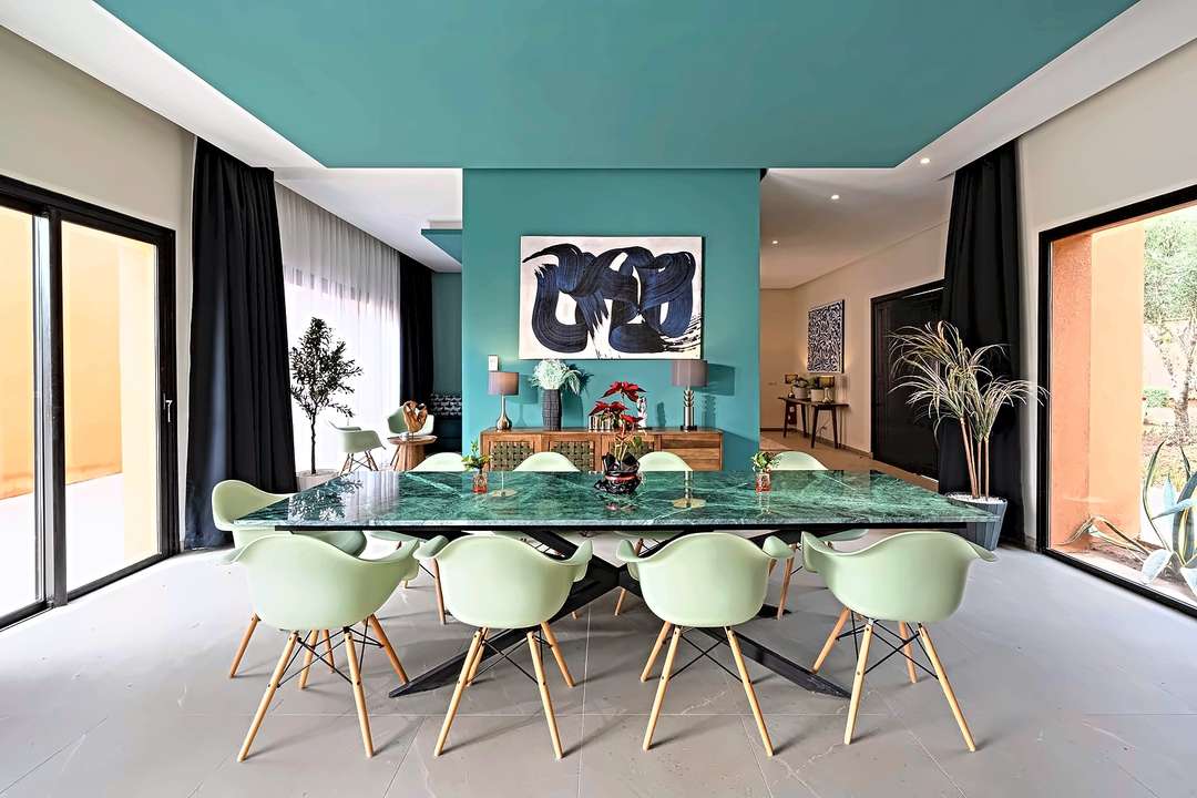 Sala da pranzo con tavolo di marmo verde per dieci, parete color petrolio e vetrate su entrambi i lati
