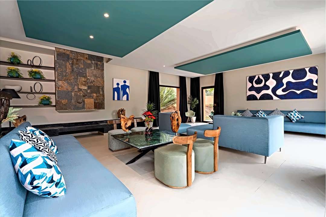 Salotto con divani blu, parete di ardesia, tavolo di marmo verde e sculture in legno di mare