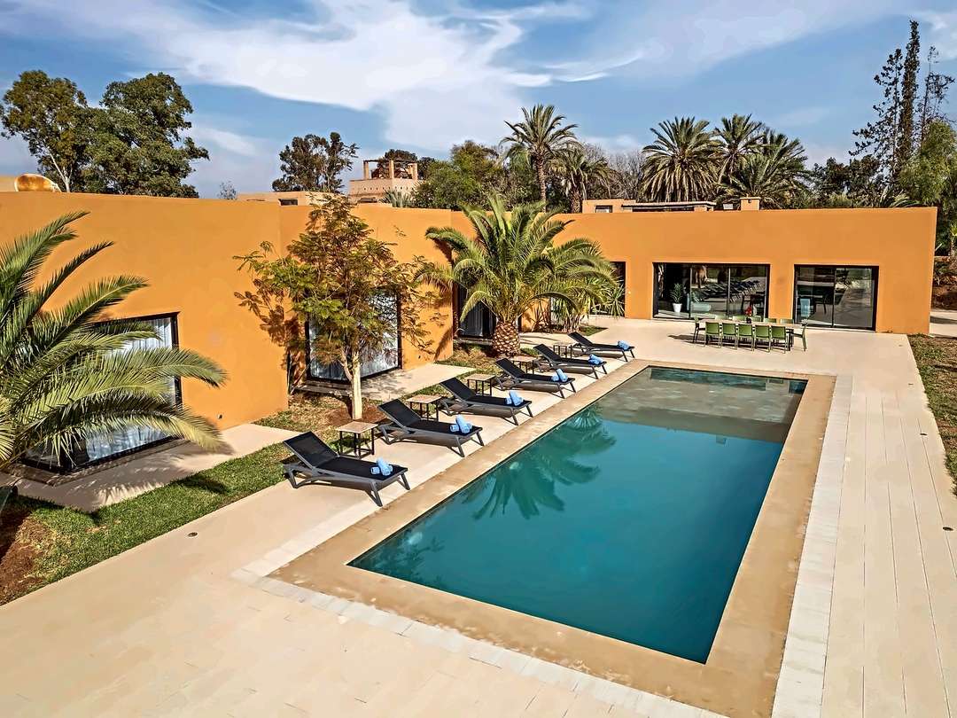 Piscina con chaise longue e tavolo da pranzo esterno per dodici, vista dall’alto sulla villa in terra ocra