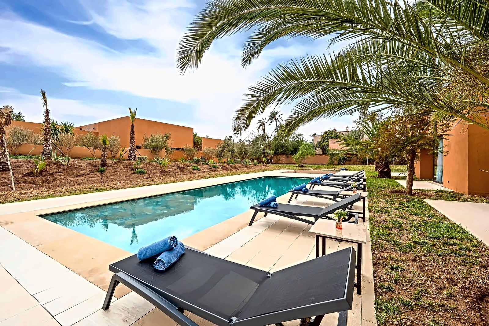 La piscina de una villa de Marrakech vista entre hojas de palmera, con la terraza y las tumbonas a un lado