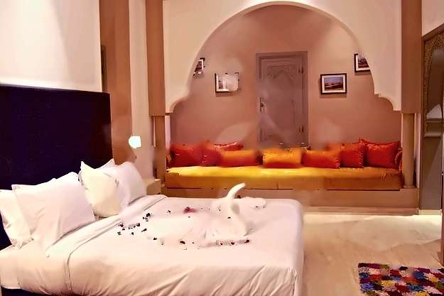 Schlafzimmer mit großem Bett und einem Bogenalkoven mit eingebauter Sitzbank und orangen Kissen
