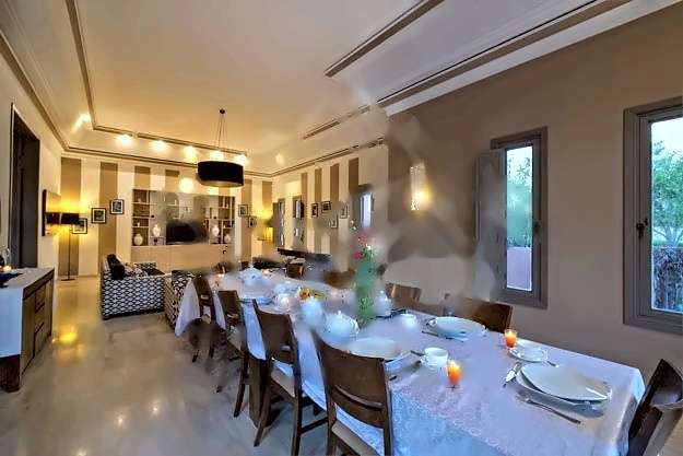 Lange Tafel für ein Abendessen gedeckt, mit Kerzen und Blumen, neben einem Salon mit gestreiften Wänden