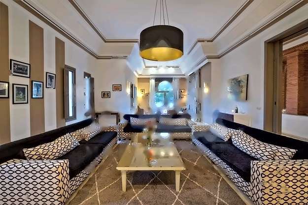 Langer Salon mit gemusterten Sofas, einer schwarz-goldenen Hängeleuchte und einem Bogenfenster am Ende