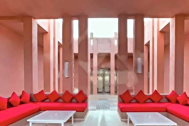 Patio-Lounge mit rosa Wänden, eingebauten Sitzbänken, roten Kissen und Zellige-Tischen unter einer Kolonnade