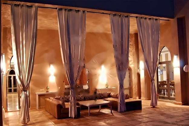 Überdachte Terrassenlounge bei Nacht, mit leichten Vorhängen, Sofas und leuchtenden Wandlaternen