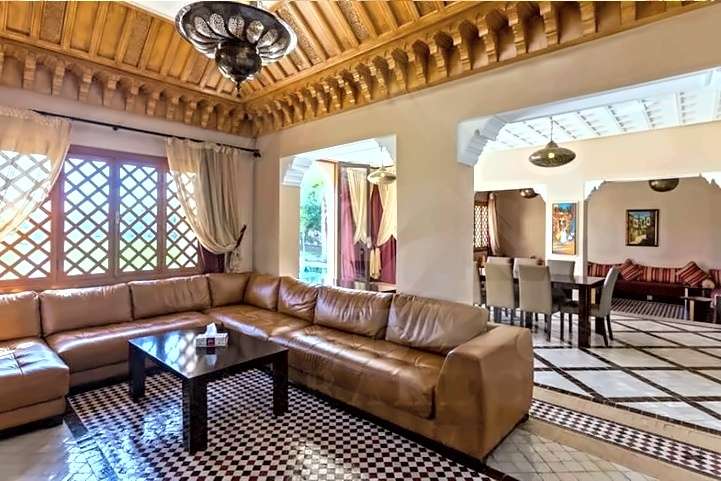 Soggiorno con un grande divano angolare di pelle, soffitto di cedro scolpito e pavimenti di zellige