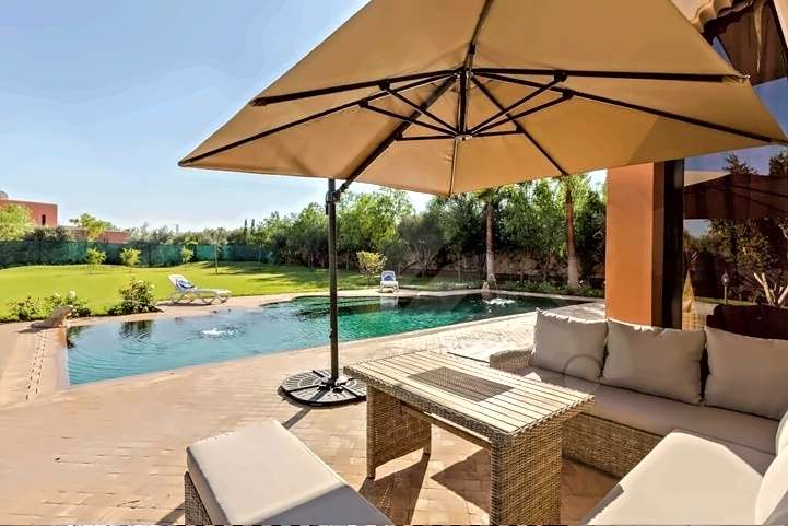 Salotto esterno con sedute in rattan imbottito sotto un grande ombrellone a bordo piscina