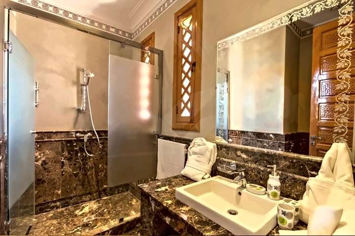 Sala d’acqua in marmo scuro, con doccia vetrata e una finestra di legno scolpito
