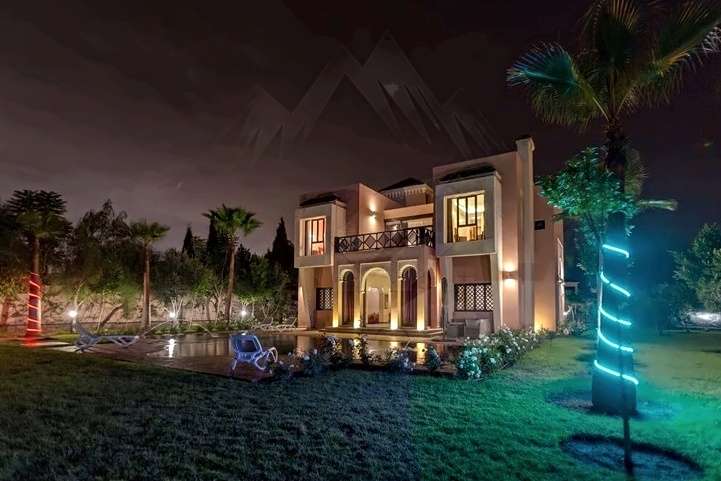 Villa e giardino di notte, con palme illuminate e la piscina al di là del prato