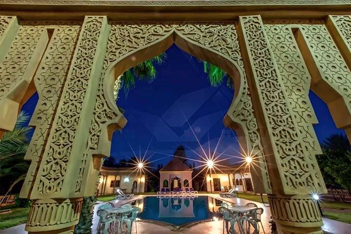 Arco di stucco cesellato che incornicia la piscina e il padiglione illuminati di notte