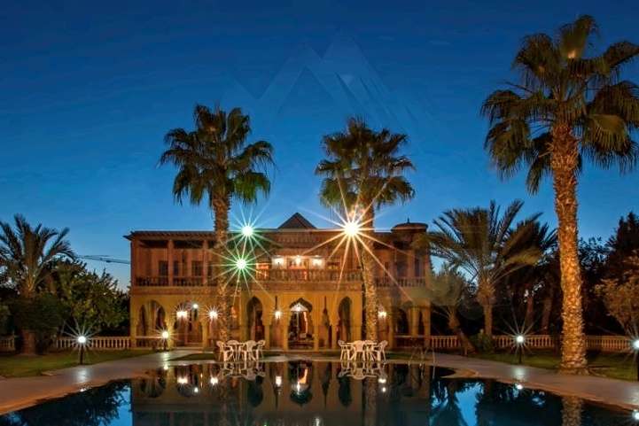 Villa illuminata di notte dietro le palme, riflessa nella piscina